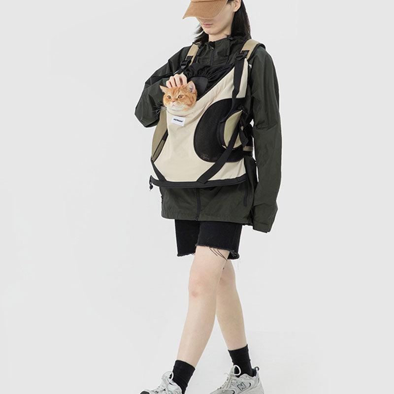 Person wearing a black jacket and shorts, holding a beige pet carrier with a cat inside on a white background.